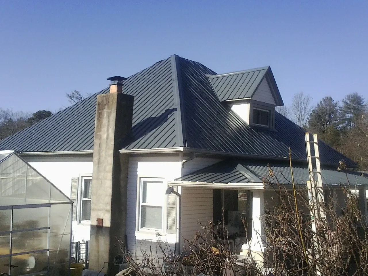 Dark blue standing seam metal roof on a white farmhouse with dormer — Slate & Tile Roof Repair by Roofing Brothers in Ona