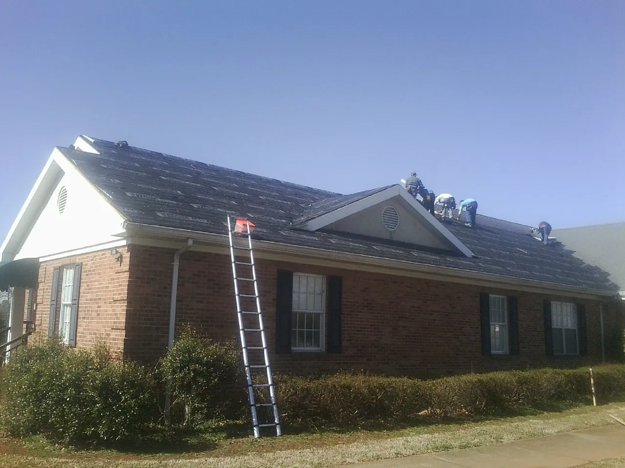 Crew tearing shingles off a brick ranch roof with a ladder set — Emergency Roof Repair work by our crew in Ona