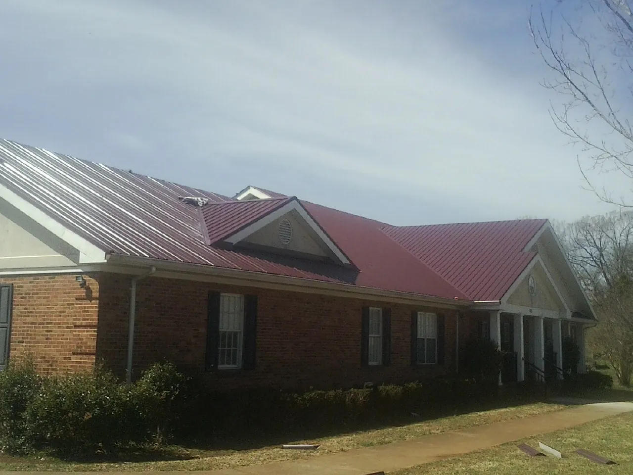 Red metal roof with gabled entries on a long brick building, from a Hail Damage Roof Repair job in Ona