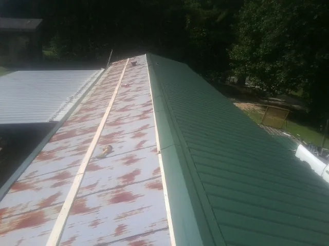 Old rusted panels beside newly installed green metal roofing — Wind Damage Roof Repair by Roofing Brothers in Ona