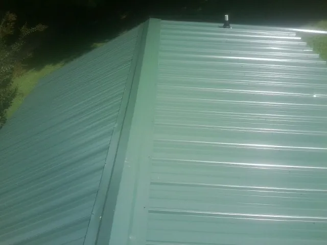 New green metal panels meeting at the ridge of a roof — Flat Roof Repair work by our crew in Ona