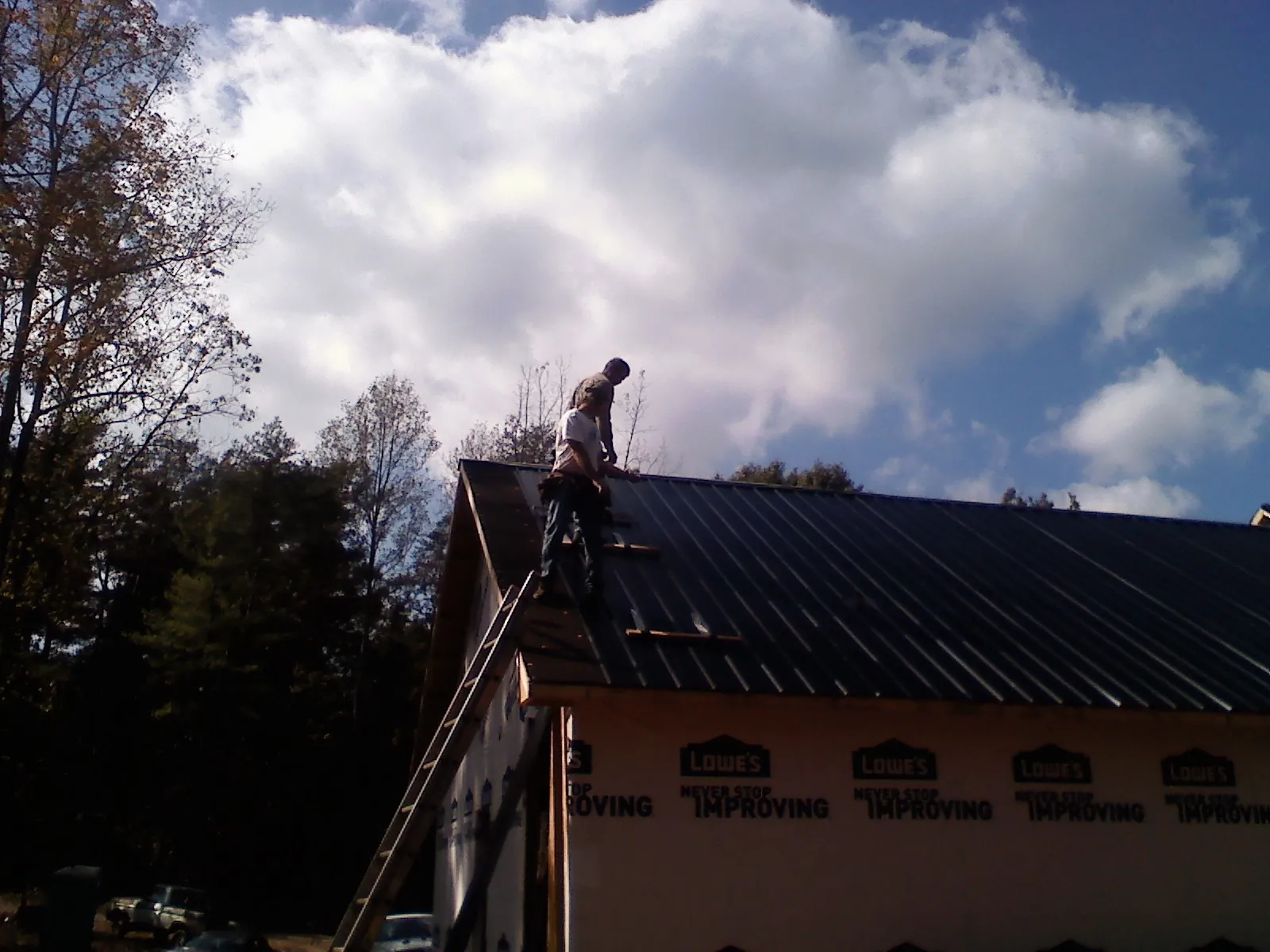 Roofer fastening dark metal panels high against a cloudy sky, from a Roof Inspection job in Ona