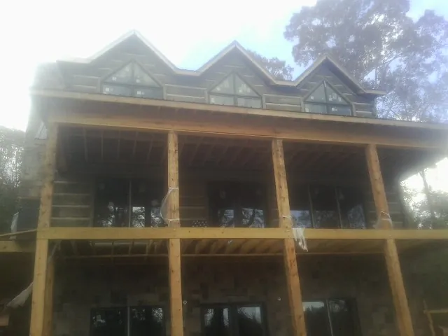 Dormers and porch framing on a large log home under construction — Roof Coating work by our crew in Ona