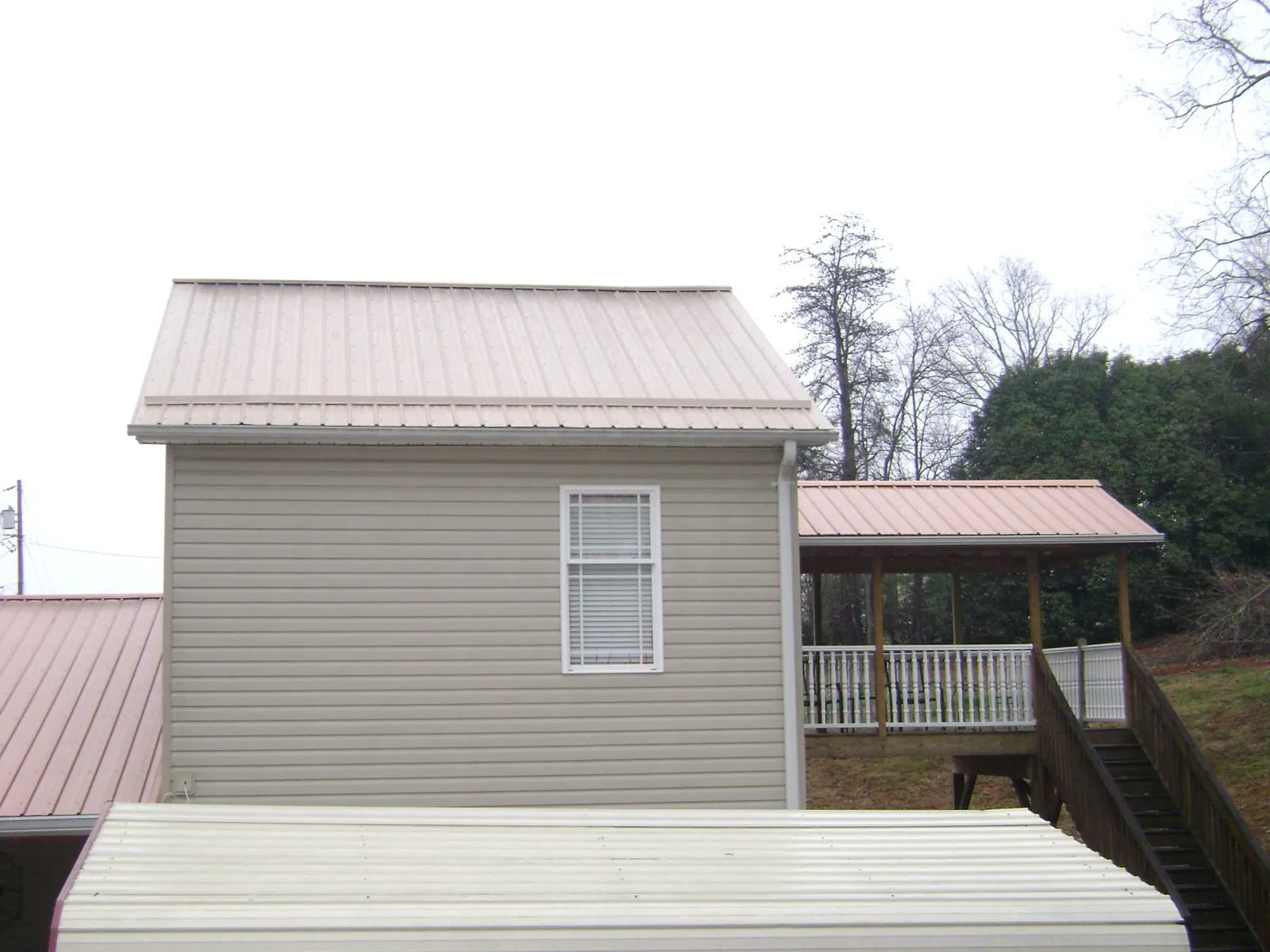 Tan metal roofs on a two story addition and attached porch, from a Roof Replacement job in Ona